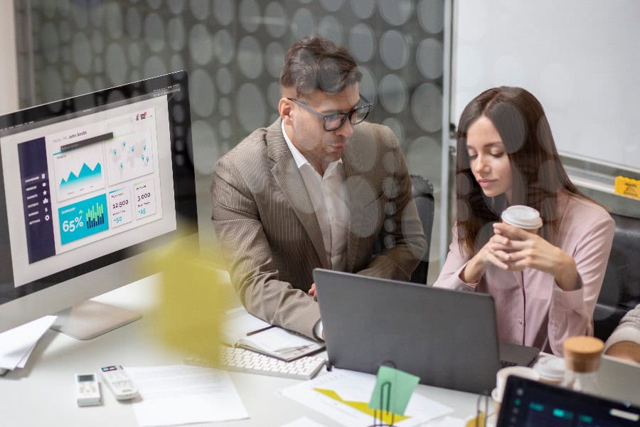 Two people reviewing leads on a laptop, with a large screen displaying data charts.