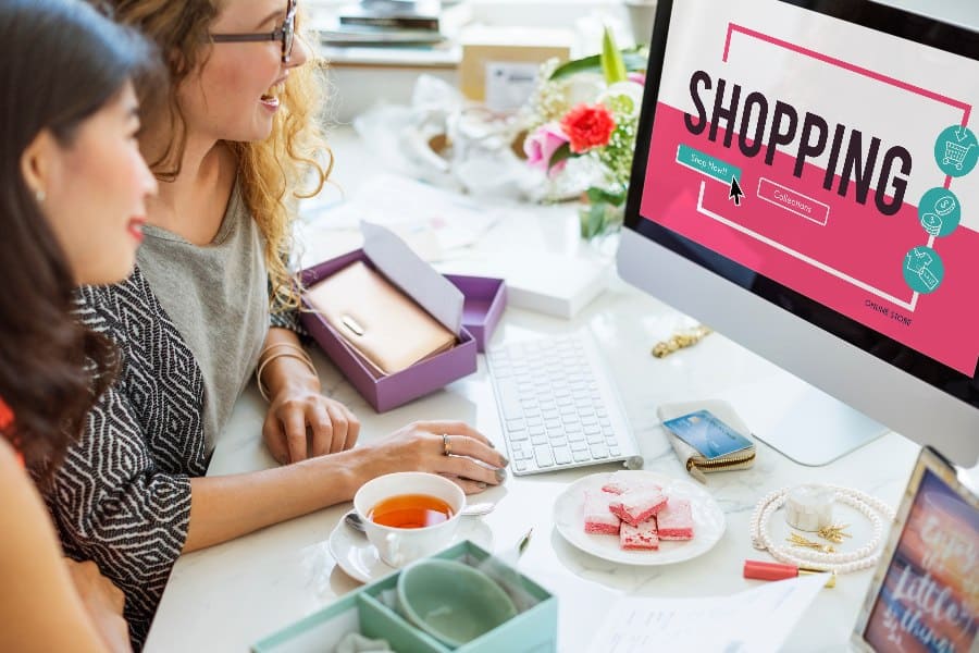 Two women shopping online together, viewing a personalised e-commerce interface on a desktop screen with vibrant visuals and product options.