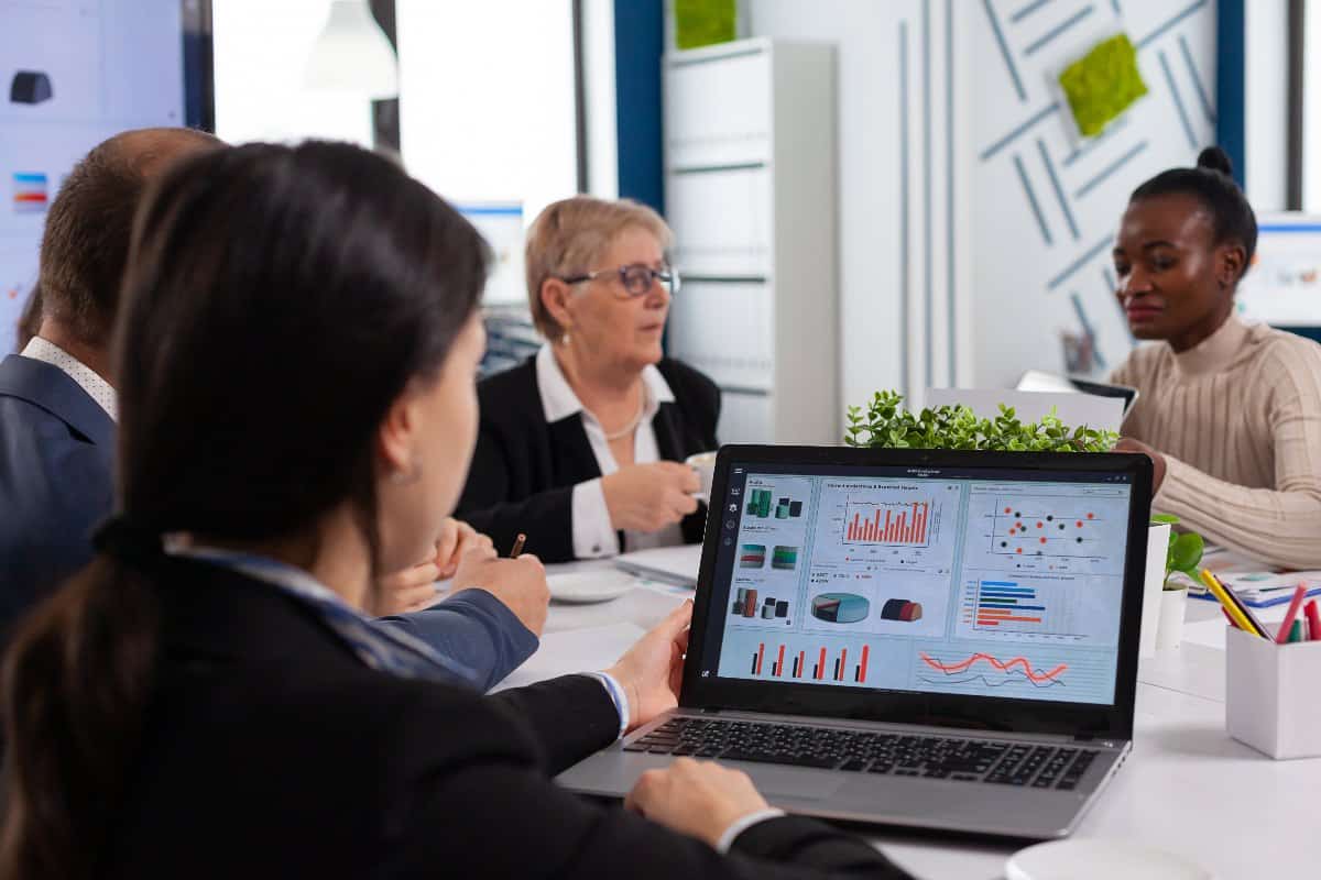 People in a meeting looking at charts on a laptop.